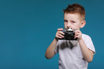 Little boy taking a picture using a retro camera. Child boy with vintage photo camera isolated on blue background. Old technology concept with copy space. Child learning photography - Powered by Adobe