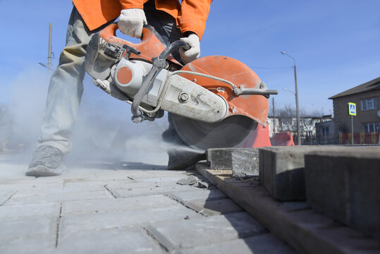 A worker saws a concrete block with a circular saw, laying paving slabs.