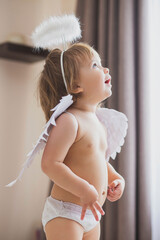 Adorable baby girl with wings and a halo looks up enthusiastically