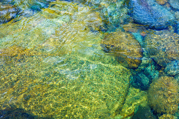 Fototapeta na wymiar Crystal clear Pemigewasset River in spring. Multi-colored stones at the bottom. Water whirlpools of Franconia Falls at the Lincoln Forest Trail in the White Mountains National Forest, NH