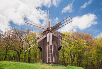 Fototapeta na wymiar Antique wooden windmill on a hill near the forest. Autumn rural landscape