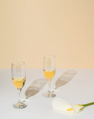 Pair of wine glasses and white calla lily flower on champagne colored background. Elegant celebration composition.