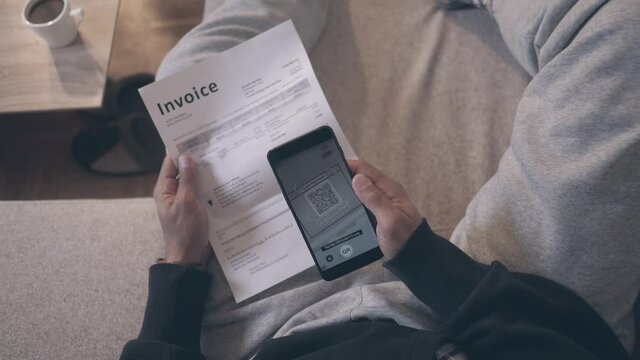 POV shot of a man casually dressed in half lying pose on a sofa, using an e payment on the smartphone to pay a bill