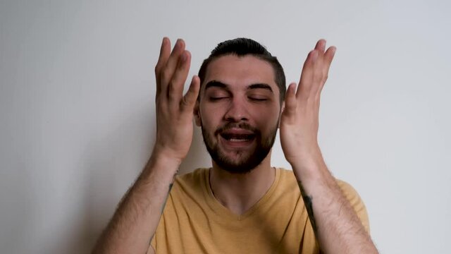 Young handsome European Caucasian man with beard shouts no and grabs his head with both hands. Person depicts the emotions of anger on white background.