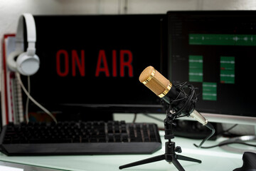 Mesa de trabajo de Blogger, con micrófono y computadora para transmisión de podcast en lineá, con anuncio al aire y monitores