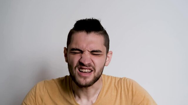 Young handsome European Caucasian man with beard shouts no and grabs his head with both hands. Person depicts the emotions of anger on white background.
