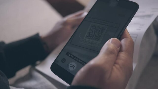 Close up of a male hand holding smartphone, making bill payment transaction via QR code reader and mobile paying app