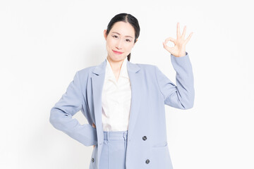 白背景の前に立って、OKのジェスチャーをする女性