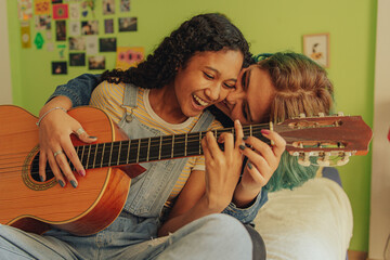 Pareja de jóvenes lesbianas tocan juntas una guitarra en su habitación 