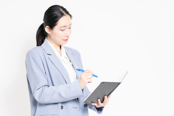 白バックの前に立って、ノートにメモを書く女性