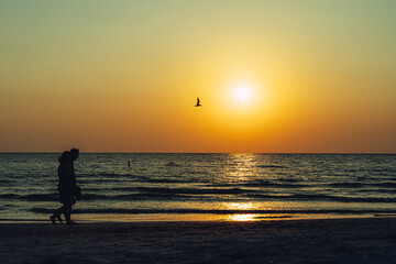 Fototapeta na wymiar Two people walk along the beach in silhouette at sunset against orange sky