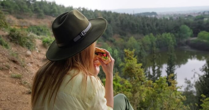 Young traveler woman taking a break during hiking and eating sandwich with scenic landscape view.
