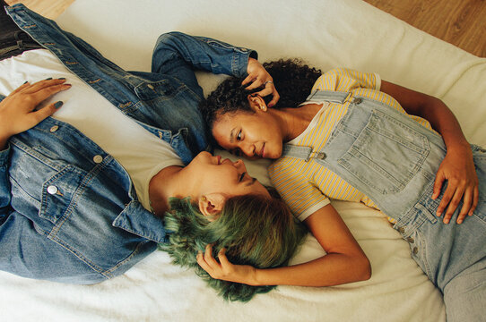 Pareja de j&oacute;venes lesbianas se miran y acarician mientras se encuentran echadas en la cama