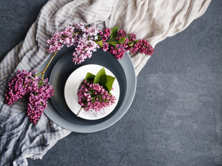 Spring festive background with purple lilac flowers in a white cup on round gray plates and...