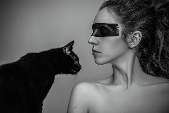 Grayscale shot of a female with tribal face paint next to a black cat