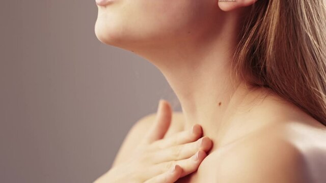 Beauty spa. Female body treatment. Sensitive skin. Delicate care. Unrecognizable profile elegant woman tenderly touching neck zone naked shoulder with hand isolated beige slow motion.