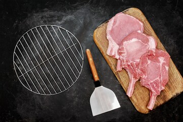 Raw Pork Bone Steaks and Grill Cooking Tools On Wooden Chopping Board. Tomahawk Pork Steaks On...