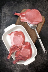 Raw Pork Bone Steaks In White Ceramic Tray and Grill Cooking Tools On Wooden Chopping Board....