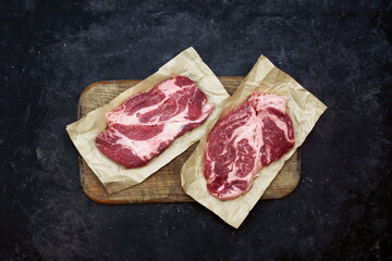 Raw Marbled loin Beef Steaks On Wooden Cutting Board. Sirloin Beef Steaks, Overhead View. Many Raw Striploin Steaks from Marbled Beef on Black Background, Top View.