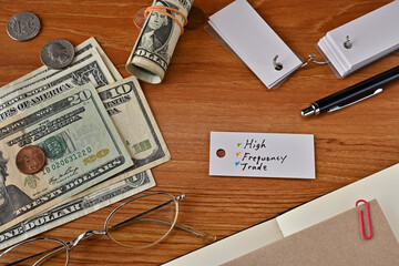 There is a word book with the word High Frequency Trade which is a financial term written on it. It is on a desk with bills, glasses and notebook.