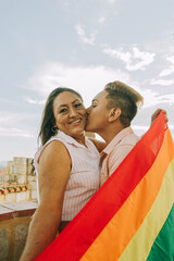 Retrato detalle de Joven gay besando a su madre mientras ella sostiene la bandera LGTBQ  - obrazy, fototapety, plakaty