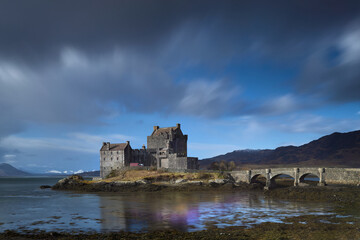 Fototapeta premium Scottish castle on lake with reflections in the water and cloudy sky. Eilean Donan