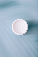 Open white container with cosmetic cream on blue background with shadows. Cosmetic moisturizing product.