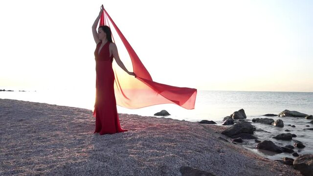 Girl in a red floaty robe standing on the beach sunset golden hour silhouette