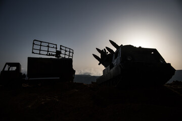 Fototapeta premium Creative artwork decoration. Silhouette of mobile air defence truck with radar antenna during sunset. Satellite dishes or radio antennas against evening sky.