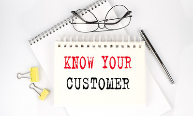 KNOW YOUR CUSTOMER text on the notebook with pen,clips and glasses