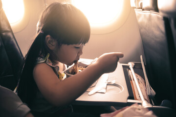 Adorable Asian young girl traveling commuting on plane airline transportation enjoying eating a...