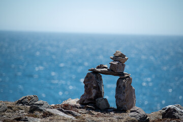 Inukshuk, a stack of granite rocks in the form of a person. The formation is a symbol of direction. The Inuit traditional figure is high on a hill. The background is a blue sky with some clouds. 