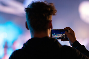 Sylwetka chłopaka, który trzyma w ręce smartfon i nagrywa przedstawienie, koncert. Używanie...