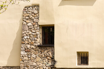 Plastered wall with masonry. Combinations of old stone and plastered walls with windows. Windows with bars in an old house.