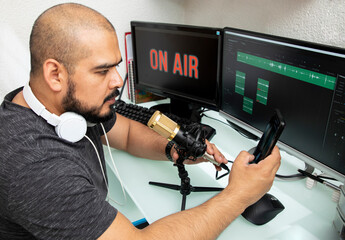 Hombre latino haciendo una transmisión en lineá de un podcast, usando un micrófono y su...