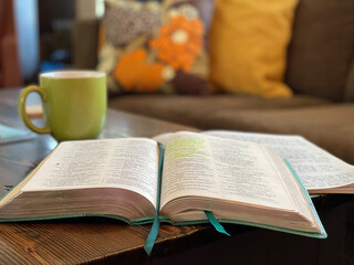Bible open on coffee table with lime-green coffee mug and couch pillows out of focus in background