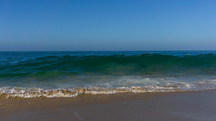 Fototapeta na wymiar Wave about to crush onto sandy beach under blue sky