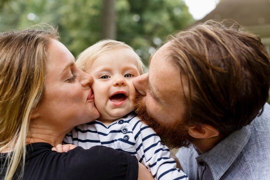Mother and father kissing baby girl on cheek, outdoors