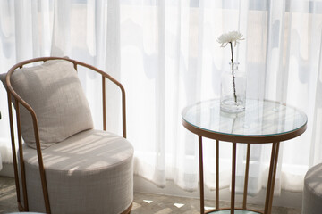 Wooden chairs and cushions with a backrest. There is a table in front of the top is clear glass and a flower vase. All are arranged by the window to let the light come in beautifully 