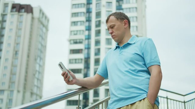 Portrait of a young man with a mobile phone in his hands, stands on the stairs, buildings background