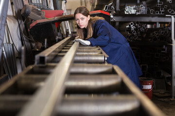 Qualified focused workwoman inspecting shape of steel stocks in metal cutting workshop....