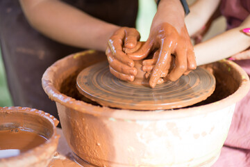 Master class for the child. Teacher hands show to kid how make ceramics dishes on potter wheel. Artist works with clay. Little girl sculpt cup clay