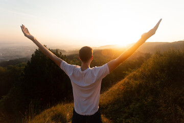 Silhouette of young man raises his hands up to sunset or sunrise on on top of hill in the summer 