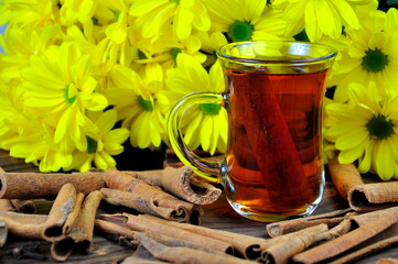 Tea with cinnamon on the table against the background of yellow chrysanthemums.