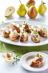 Pear and prosciutto crostini appetizers on a platter with a serving of one in front and pears in behind.