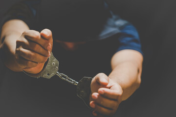 Young man of prisoner hands in handcuffs on black background.