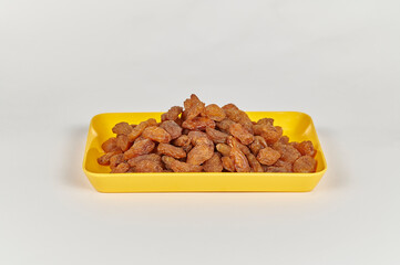 Indian brown raisins (Vitis vinifera) or Munakka on a yellow plate against a white background