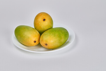 Three Dassehri mangoes on a white plate against a white background