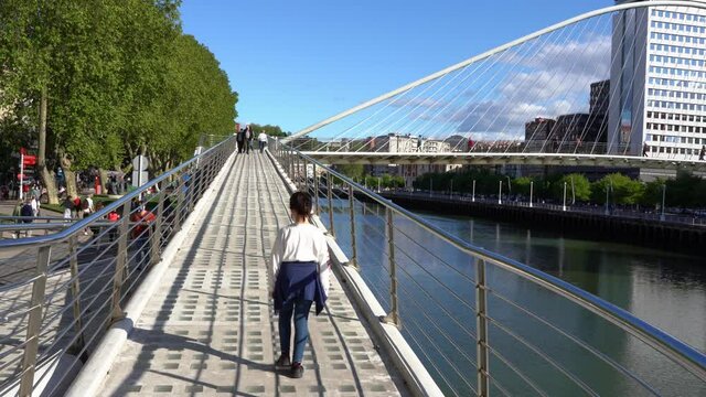 Little girl walking alone on bridge ramp by Nervion river in Bilbao city on sunny day