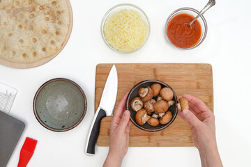Crimini mushrooms in a bowl close up on kitchen table. Pizza with mozzarella and mushrooms recipe, flat lay, woman hands